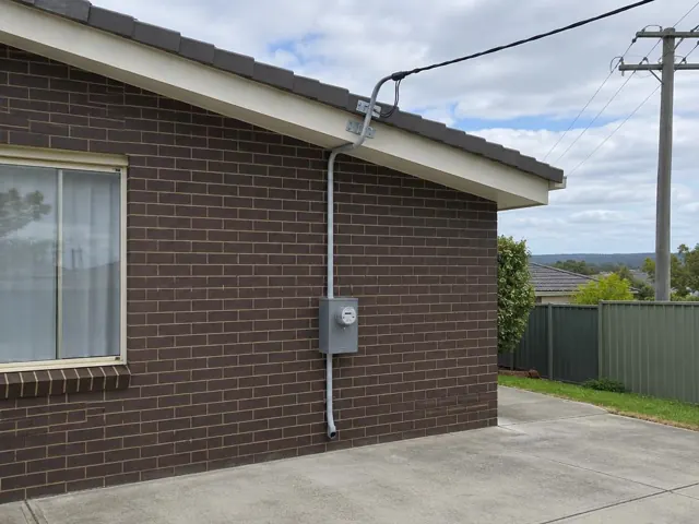 Brick house exterior with overhead service cable and point-of-attachment bracket under the eaves in Tarro